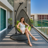 Woman sitting in a hanging egg chair on a modern balcony with a cityscape background